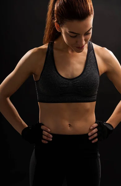 Young female athlete with tight abs against black background