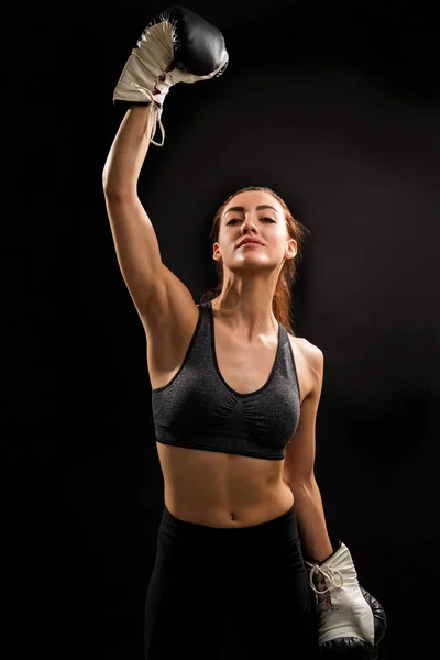 Confident young successful female boxer standing with arm raised against black background