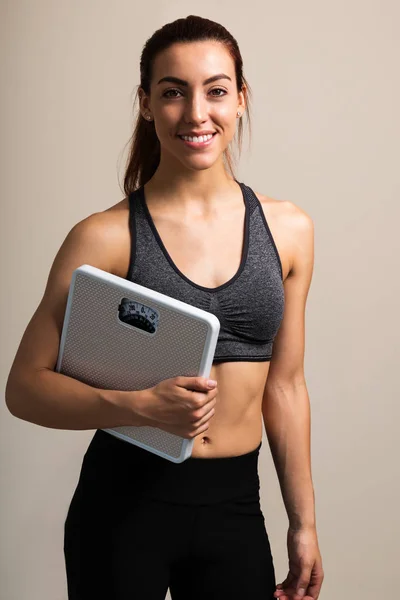 Smiling Young Female Athlete Holding Weight Scale While Standing Plain — Stock Photo, Image