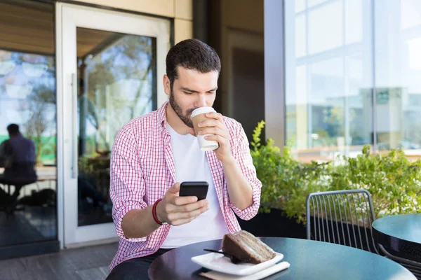 Young blogger drinking coffee while sharing story online on smartphone at shopping mall