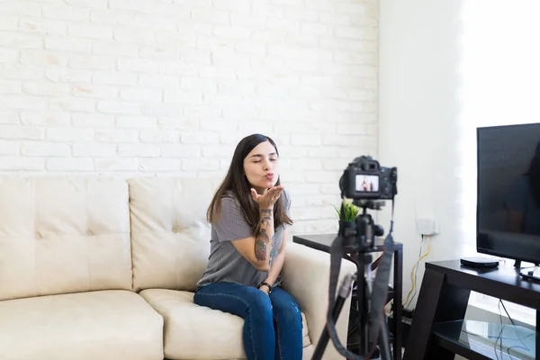 Pretty young woman recording video blog at home and blowing a kiss to her fans