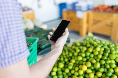 Mağazada limon için alışveriş yaparken boş ekran ile akıllı telefon tutan adam Kırpılmış görüntü