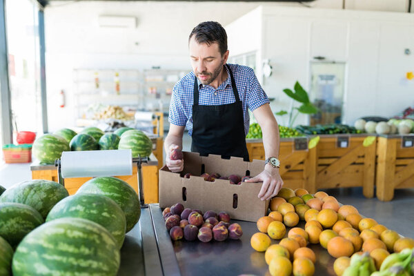 Male store manager examining organic peaches at fruit stall in supermarket