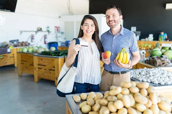 Sorrindo Bela Mulher Mostrando Cartão Crédito Enquanto Namorado Segurando Frutas — Fotografia de Stock