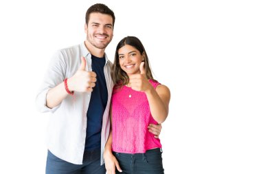 Mutlu genç kız arkadaşı ve erkek arkadaşı beyaz arka plan karşı birlikte dururken başparmak kadar gesturing