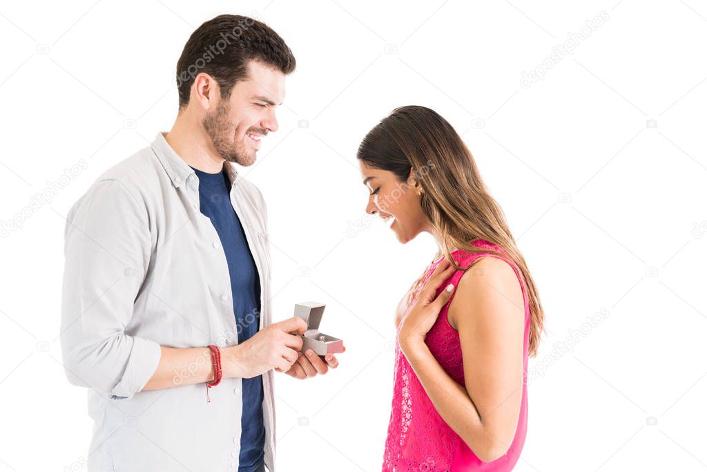 Surprised woman looking at proposal ring held by boyfriend against white background