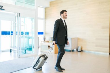 Otel lobisinde gelen Bagaj çekerek gülümseyen Ispanyol erkek girişimci tam uzunluğu