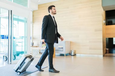 Otelde bavulu çekerken emin orta yetişkin Yöneticisi lobide yürüyüş