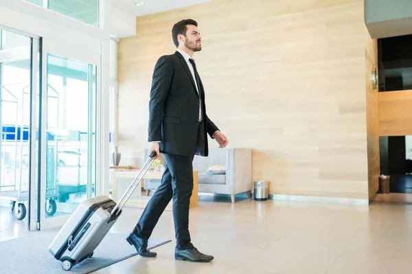ホテルでスーツケースを引っ張りながらロビーを歩く自信のある中大人のマネージャー — ストック写真