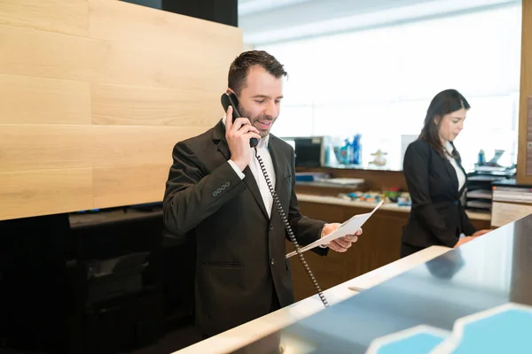 Recepcionista Masculino Adulto Médio Falando Telefone Enquanto Segurava Papel Balcão — Fotografia de Stock