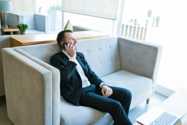 Cep telefonu konuşurken uzak görünümlü rahat erkek girişimci ve otelde kanepede oturuyor