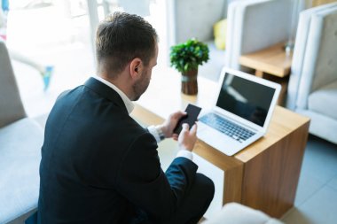 Otelde lobide laptop ile otururken akıllı telefonda işadamı metin mesajlaşma yüksek açı görünümü