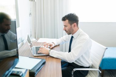 Orta yetişkin profesyonel otel odasında masada otururken dizüstü bilgisayar üzerinde iş yapıyor