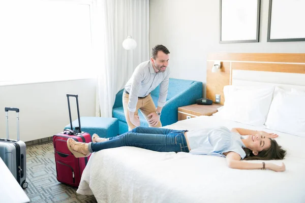 微笑的男人看着疲惫的伴侣舒适地躺在床上 享受在酒店房间度假 — 图库照片