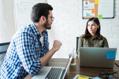 Ofiste dizüstü bilgisayarda çalışırken proje üzerinde tartışan iş arkadaşları