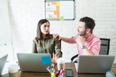 Ofiste masada dizüstü bilgisayar kullanırken konuşan İspanyol iş arkadaşları