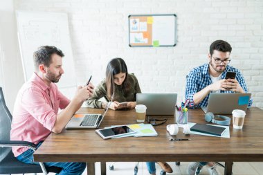 Ofiste cep telefonlarında sosyalleşme sırasında Konferans masasının etrafında oturan iş insanları