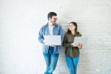 Ofis beyaz duvara eğilirken dizüstü bilgisayarlar kullanarak gülümseyen genç meslektaşları