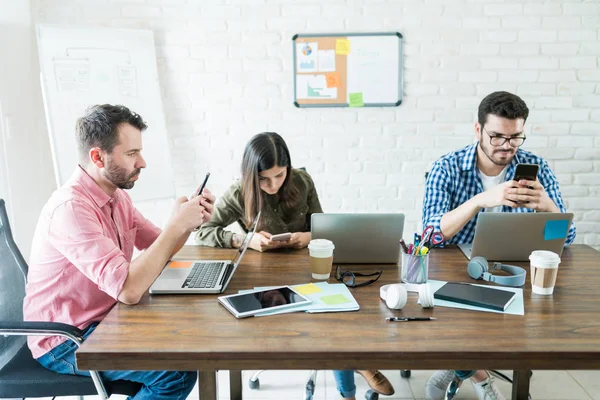 Empresários Sentados Torno Mesa Conferências Enquanto Socializam Telefones Celulares Escritório — Fotografia de Stock