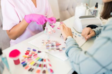 Salonda paletten çeşitli tırnak renkleri seçiminde çalışan yardımcı müşteri
