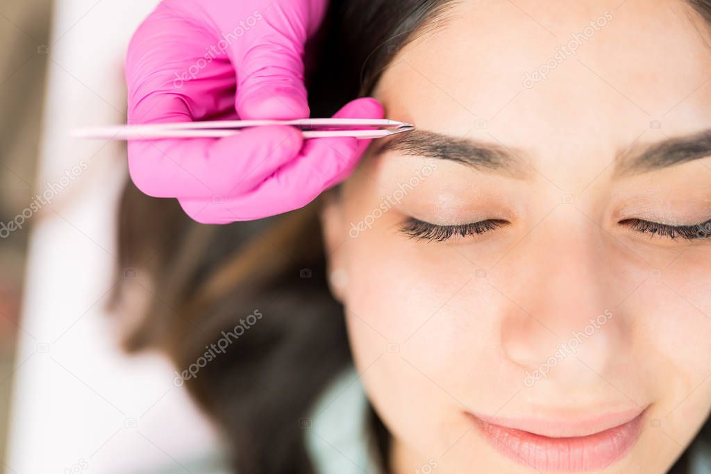 Latin female with eyes closed getting her eyebrows in shape at salon