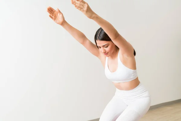 Pretty Caucasian woman practicing chair pose against wall in fitness training studio