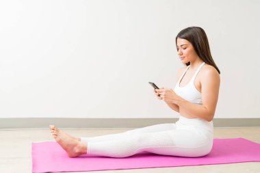 Yoga minderinde otururken mobil üzerinden rahat güzel Kafkas genç kadın metin mesajlaşma