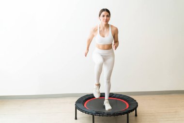 Yüksek yoğunluklu aralıklı eğitim sırasında duvara karşı trampolining beyaz spor giyim adanmış genç kadın