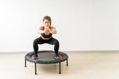 Fitness eğitim egzersiz sırasında stüdyoda duvara karşı çömelme yaparken Pretty genç esmer kadın trampolining