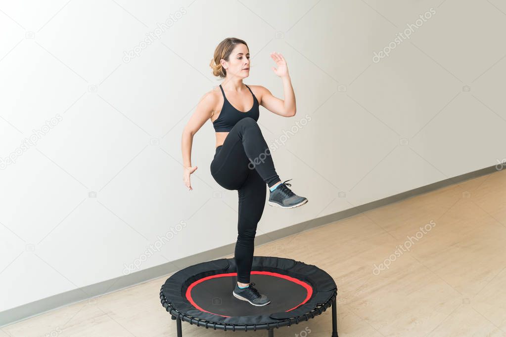 Energetic young woman in sportswear trampolining against white wall during high intensity interval training