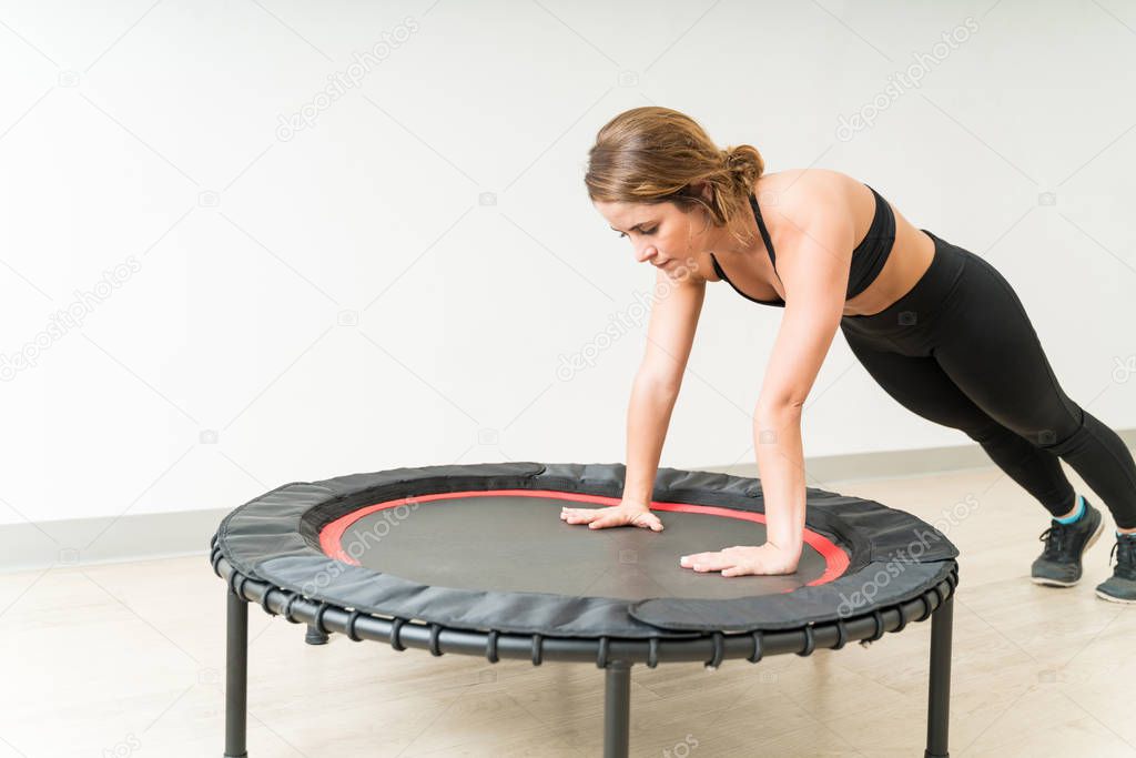 Confident young brunette woman exercising on mini trampoline during high intensity interval training