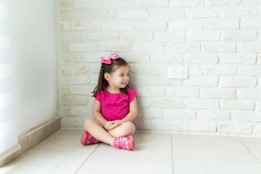 Evde oturma odasında beyaz duvara karşı otururken uzakta bakan gülümseyen kız tam uzunlukta