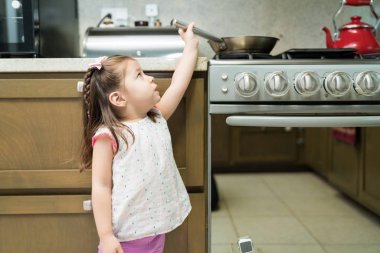 Evde mutfakta fırın ın yanında dururken tencereye uzanan küçük kız