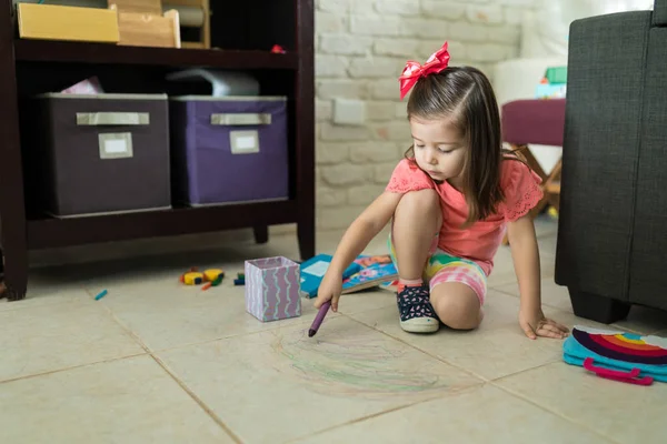 可爱的小女孩画与五颜六色的蜡笔在瓷砖地板上在家里 — 图库照片