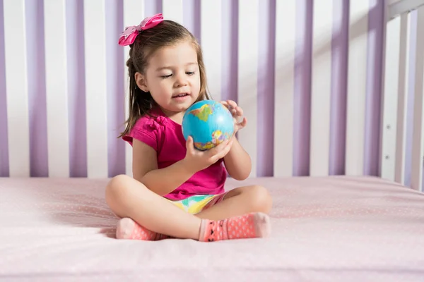 自宅で寝室でベッドの上にグローブボールを見て魅力的な遊び心の幼児 — ストック写真