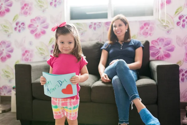 Sorrindo Menina Mostrando Cartão Saudação Enquanto Mãe Fundo Casa — Fotografia de Stock