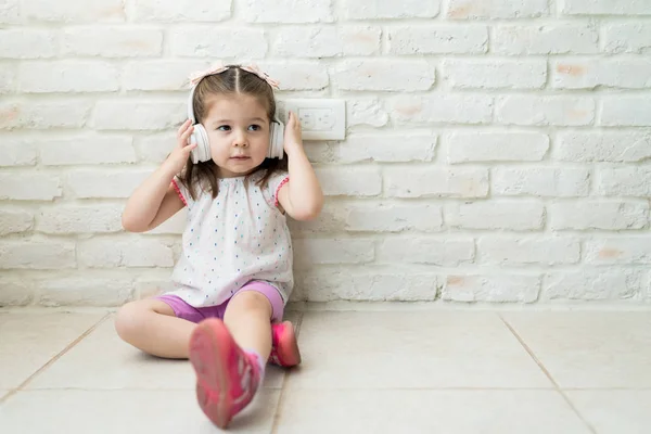 自宅で壁に座っている間 ヘッドフォンを通して音楽を聴く幼児 — ストック写真
