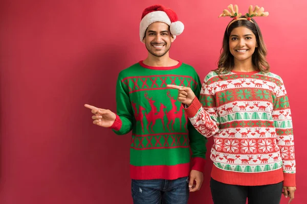 Güzel kadın ve yakışıklı adam kırmızı arka plan üzerinde boş alanı işaret ederken gülümseyen