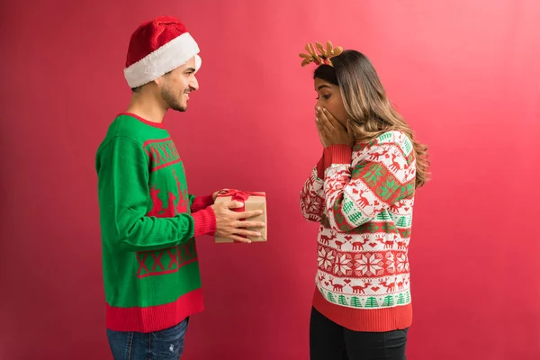 Sade arka plan aleyhine Noel hediyesi ile ayakta erkek arkadaşı bakarken ağız kapsayan sürpriz kadın