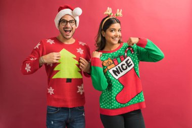 Neşeli İspanyol çift stüdyoda izole Xmas kutlama sırasında çirkin kazak gösteren