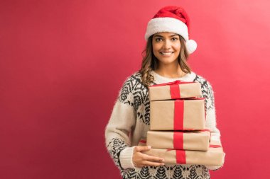 Noel sırasında hediye yığını ile çekici Latin kadın kırmızı arka plan karşı göz teması yapma