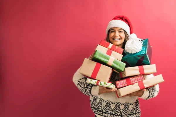 Happy attractive woman with stack of Christmas gift celebrating against plain background