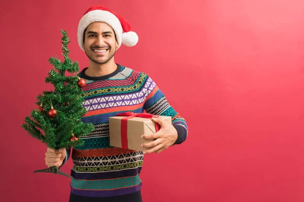 Handsome Young Hispanic Man Holding Christmas Tree Present Plain Background — Stock Photo, Image