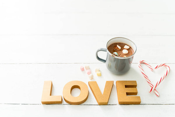 Concept of the word "LOVE" sitting on a white wooden table with candy canes, a heart shape and hot chocolate with marshmallows