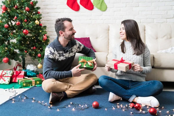 クリスマスのお祝いの間にプレゼントを持ち 自宅のリビングルームに座って話している笑顔のカップル — ストック写真