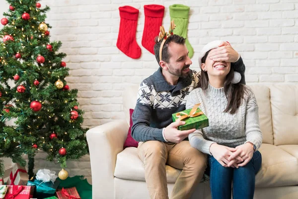 Man surprising woman with present while sitting at home during Christmas