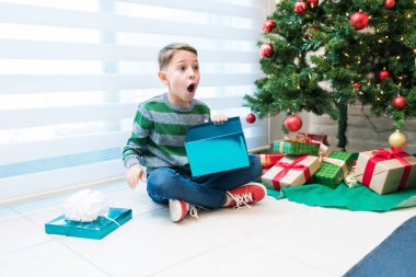Evde Noel ağacının yanında açık hediye kutusuyla oturan süpriz çocuk.