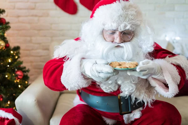 Głodny Człowiek Ubrany Santa Kostium Patrząc Ciasteczka Domu Podczas Świąt — Zdjęcie stockowe