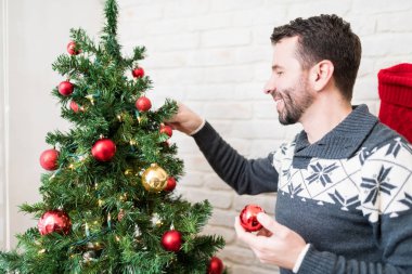 Noel sırasında evde baubles ile kazak dekorasyon ağacı gülümseyen Kafkas adam