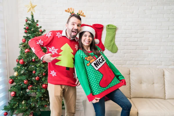 Playful partners showing their ugly sweaters while enjoying Christmas holiday at home